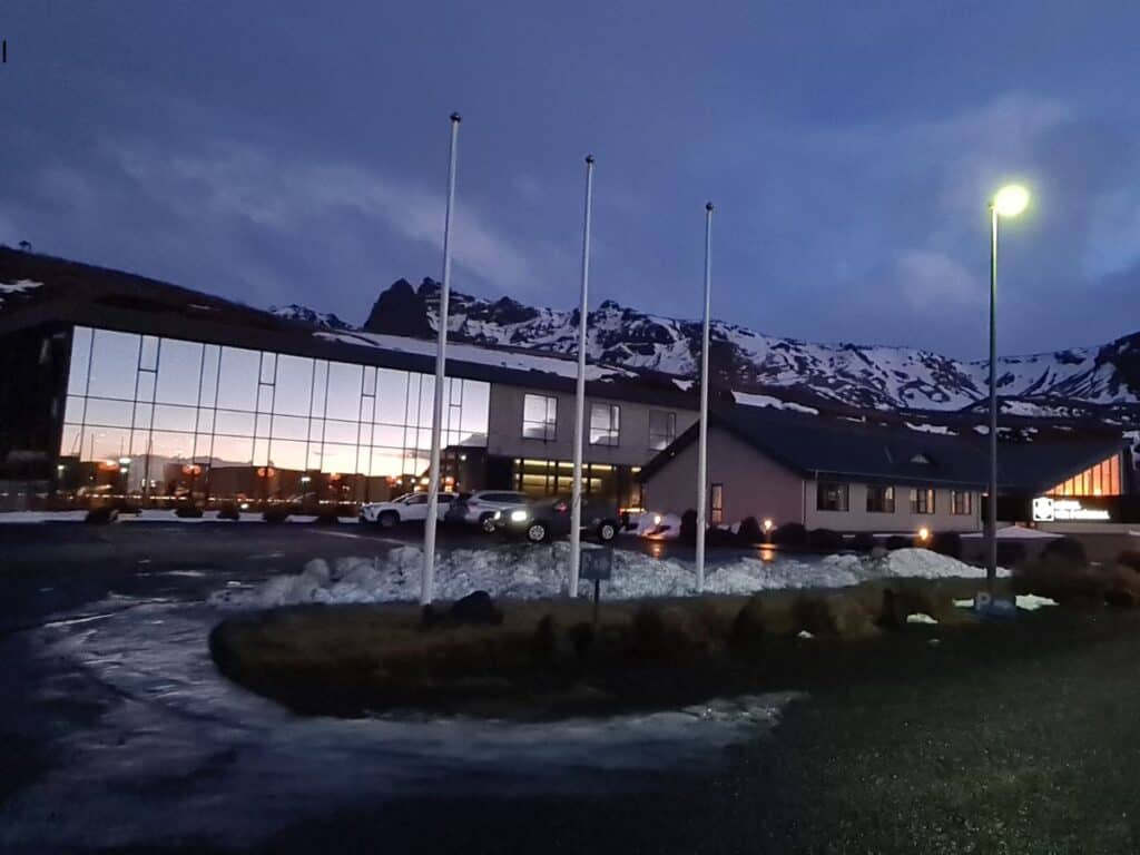 Large glass fronted building surrounded by snowy mountains and three empty flag poles in Vik Iceland.