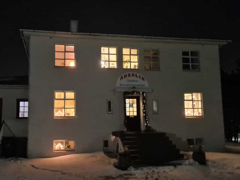 White hotel to stay in Vik with lights on at night surrounded by snow.