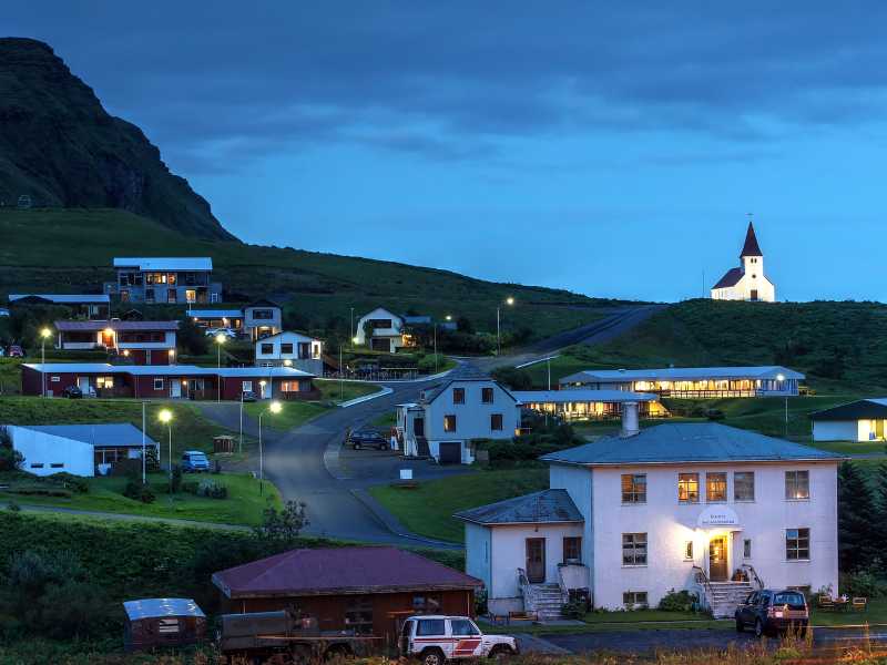 Mountain town lit up at dusk with a church on the hill.