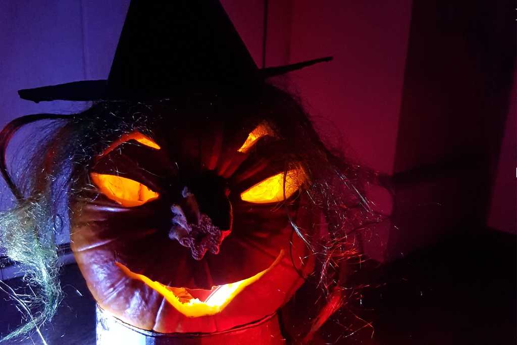 A illuminated carved pumpkin with hair and hat for Halloween.