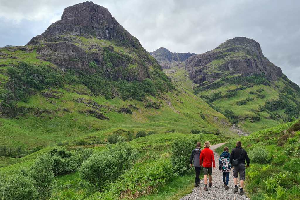 A family walking on a path towards iconic green hills in Scotland in summer for an adventure.