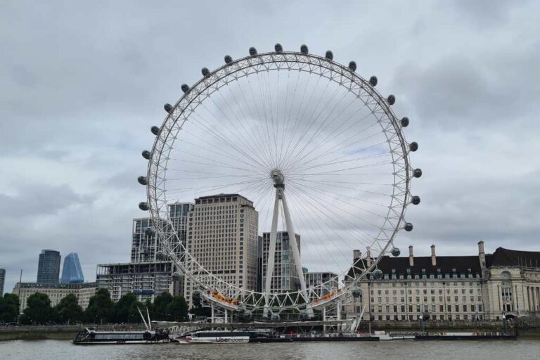 A large iconic Ferris wheel next to a river on a cloudy day.