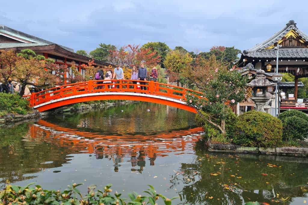 Red bridge over a pond with people stood on in a Japanese garden in Kyoto Japan.