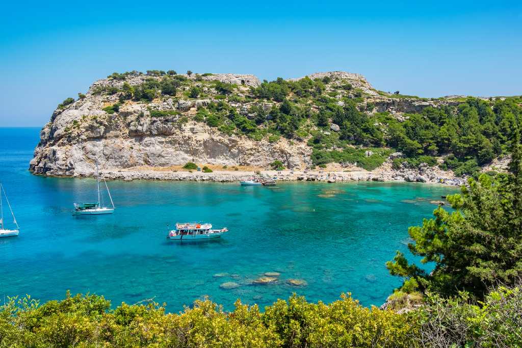 Boats in a bay of clear water surrounded by rocks in Greece. Arsty - Getty Images