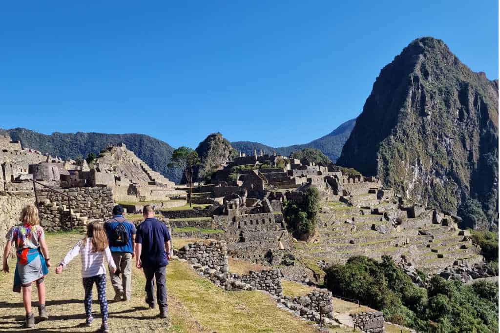 A family walking through ruins on a hill with towering cliffs in Machu Picchu, Peru as a bucket list adventure to one of the wonders of the world.