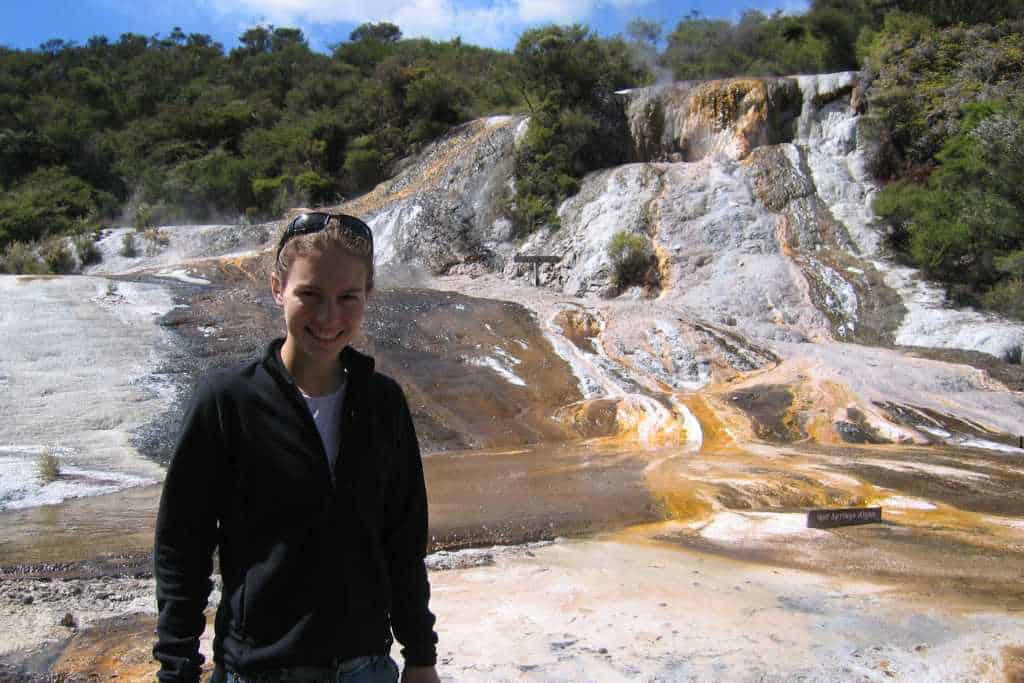 A person stood at a geothermal park with liquid coming down rocks. This is a top place to visit while road tripping New Zealand. 