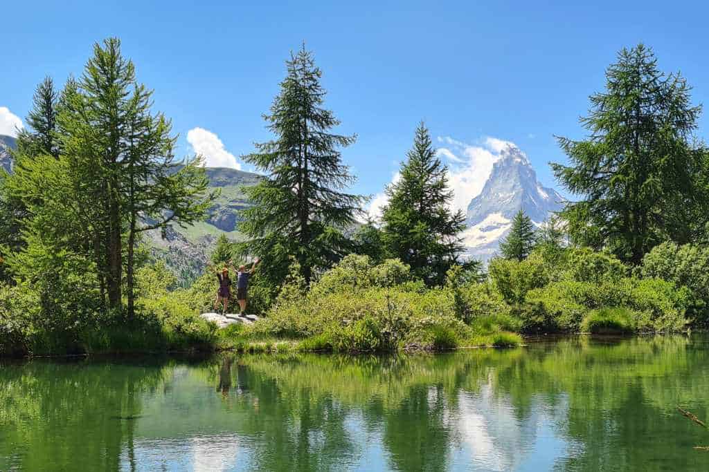 Kids stood across a lake with the distnat snowy mountains and trees reflecting in the water. Switzerland is a bucket list destination for families.