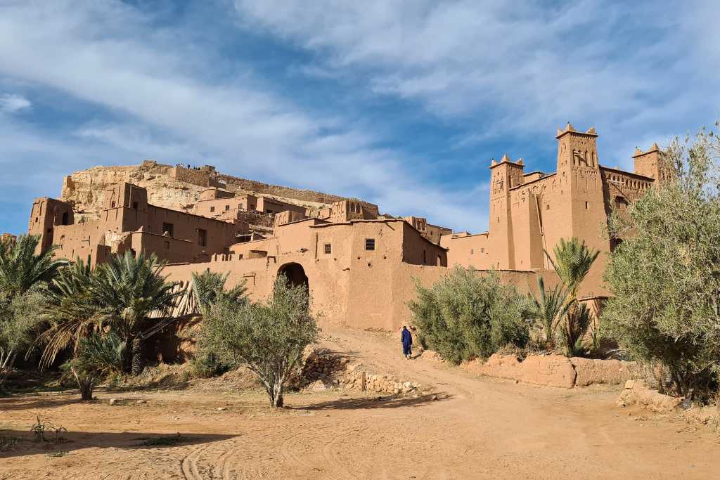 The entrance of a mud built city surrounded by trees in a desert. Ait Ben Haddou is a must see kasbha in Morocco.