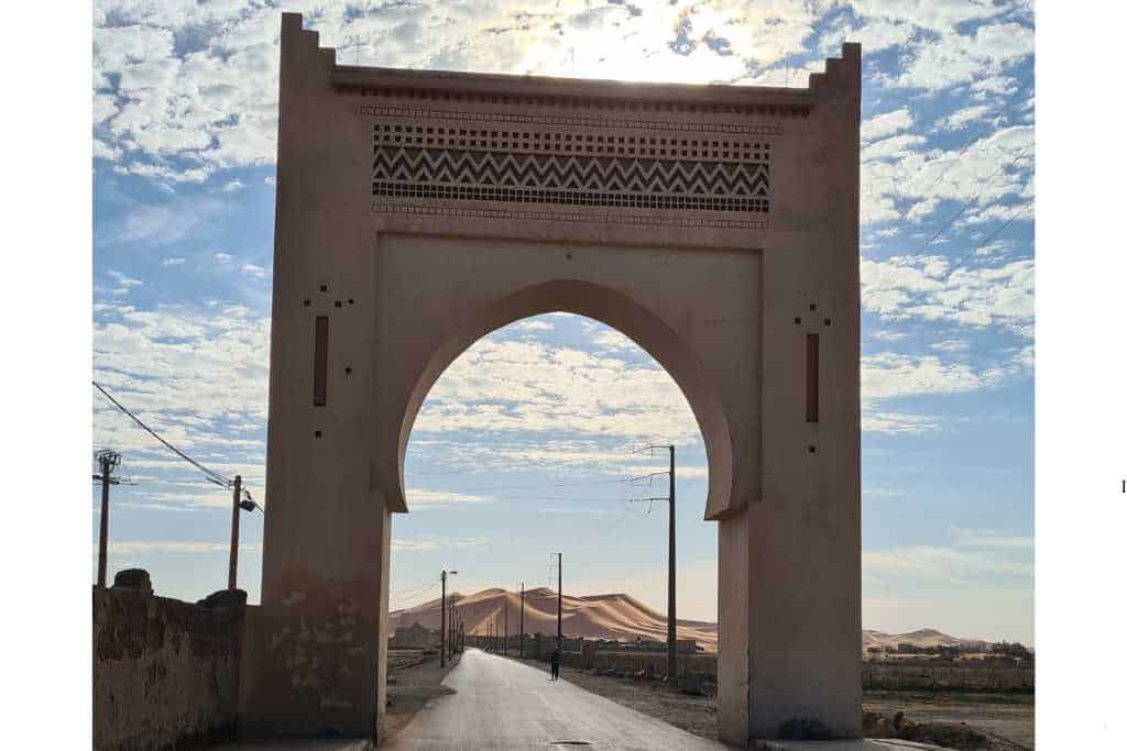 Stone arch with sand dunes marking the gateway to the Sahara in Merzouga.