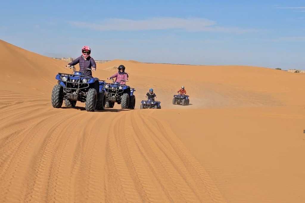 A family riding quad bikes in a line through dunes in the desert.