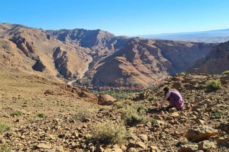 A kid inspecting rocks overlooking mountains and a town in Morocco.