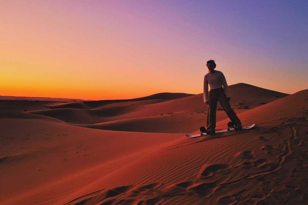 A child sand boarding down a sand dune in the Sahara Desert as the sunsets.