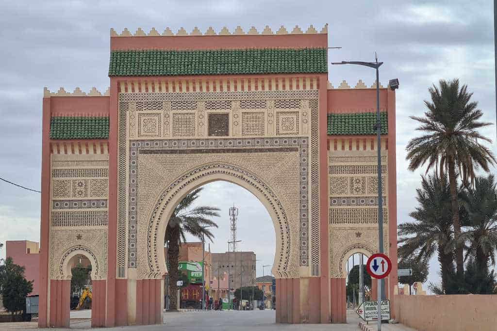 Pink, Cream and green tiled arch entrance over a road in Morocco. 