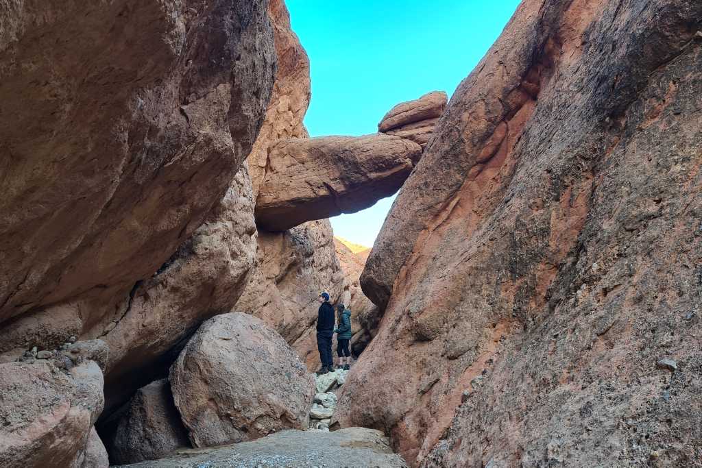 Kids exploring rock formations in a dry red rock canyon in Dades Valley, Morocco.