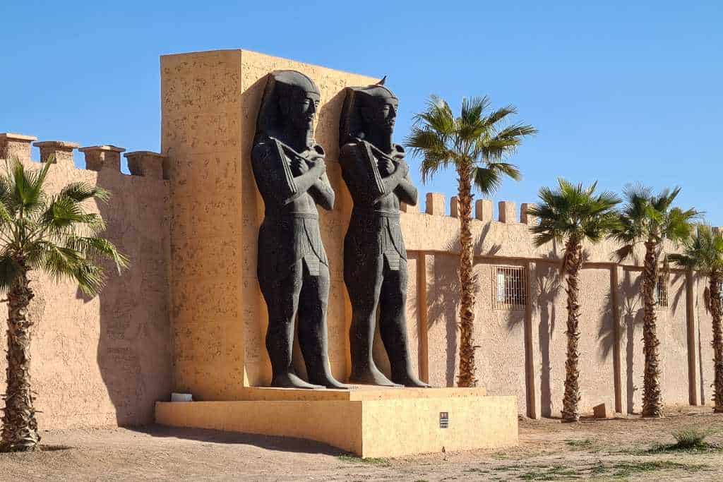 Two large statues on a platform in the desert with palm trees in Morocco.