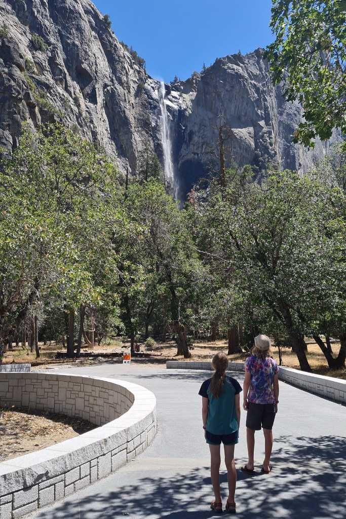 Kids stood on a path facing away looking at a tall waterfall in Yosemite National Park.