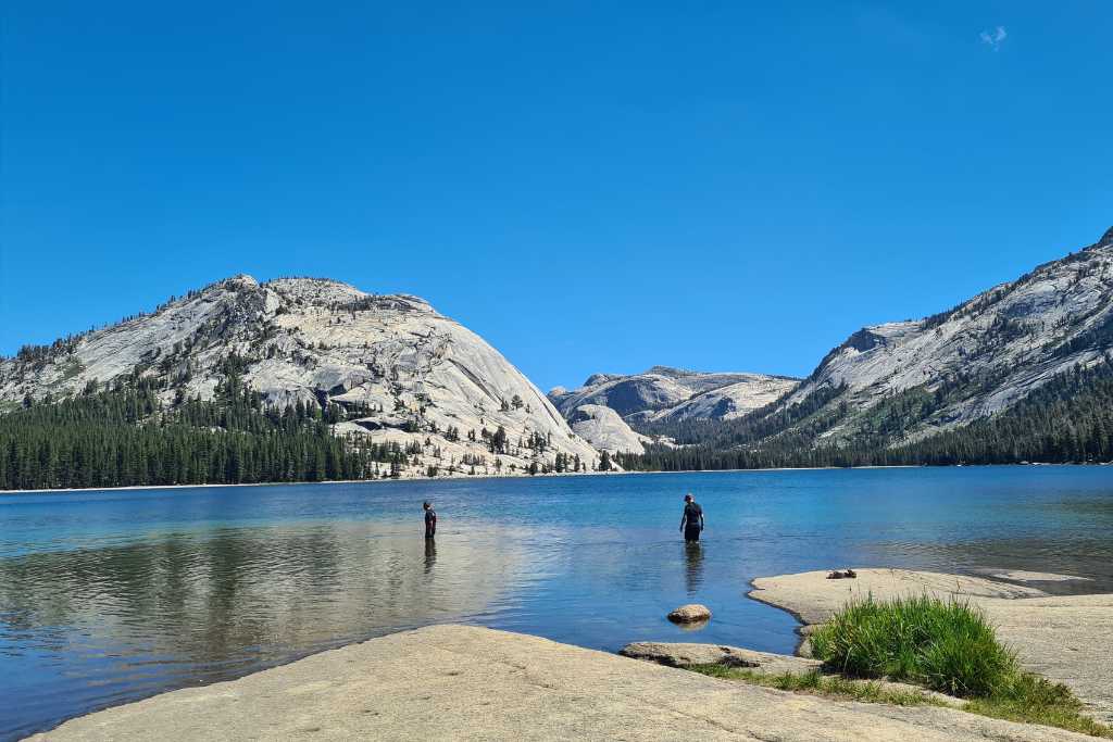 Kids in a lake with large mountains on a sunny day in Yosemite National Park.