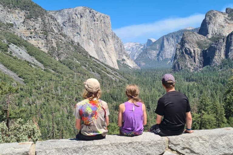 Three children sat facing away with a view of mountains in a valley at Yosemite National Park, California.