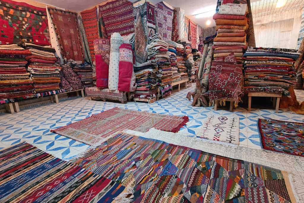 A shop with piles of colourful rugs for sale. A popular thing to buy from Morocco.