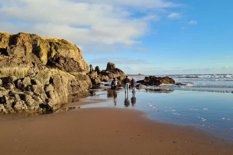 A family walking on a beach by rocks. A perfect place to visit in Scotland on a sunny day.