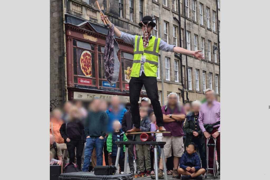A Fringe street performer balance on a table surrounded by crowds in Edinburgh.
