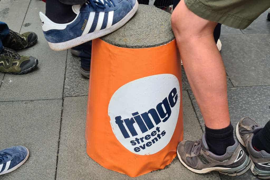 Kids resting feet on a 'fringe street events' orange bollard.