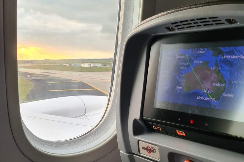An airport runway with sunset view through airplane window. The screen shows the adventure from Australia to Indonesia.