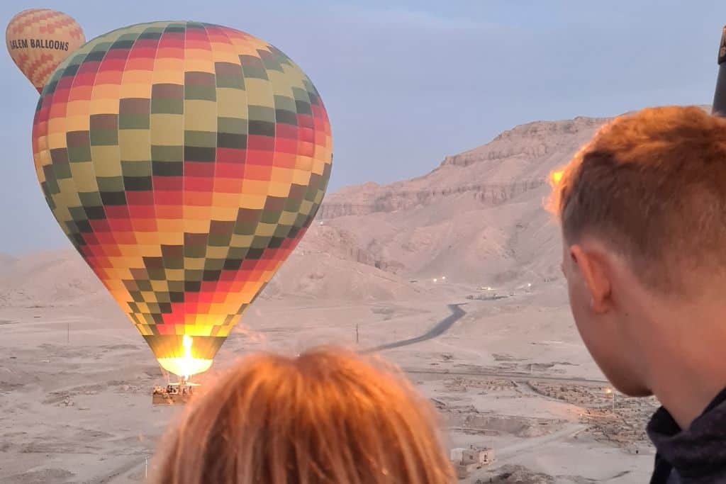 Kids watching a colourful hot air balloon going up over the Valley of the Kings in Luxor Egypt.