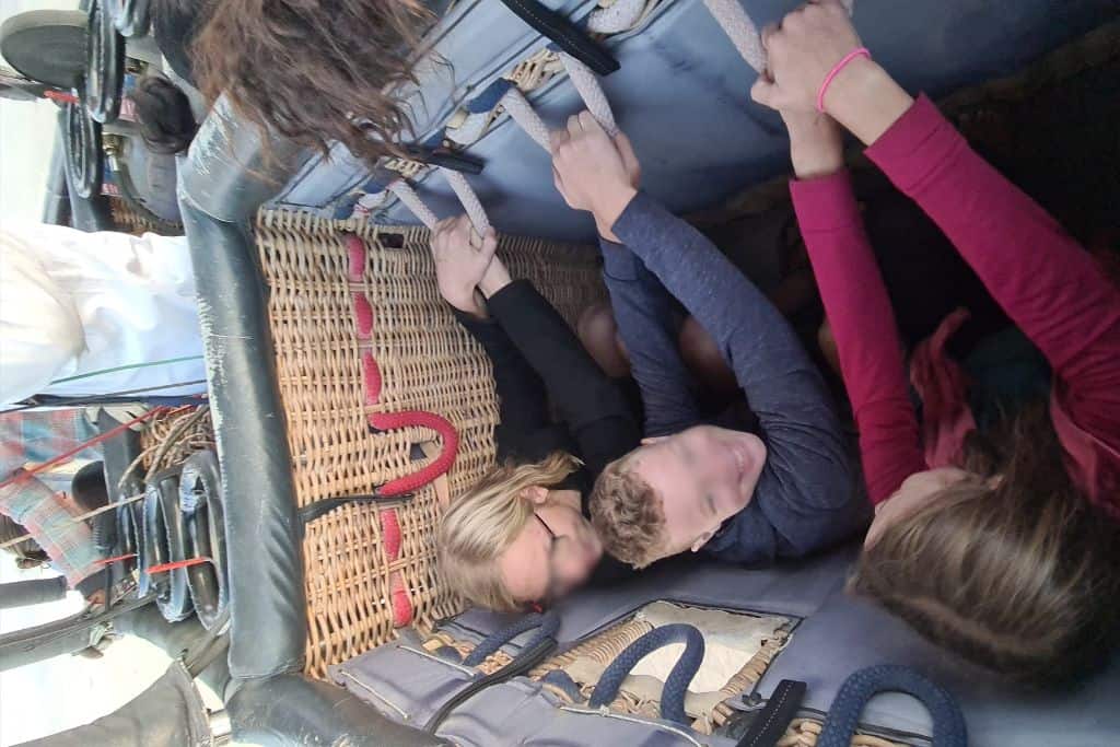 Kids excited to be riding braced in the basket of a hot air balloon on a family trip.