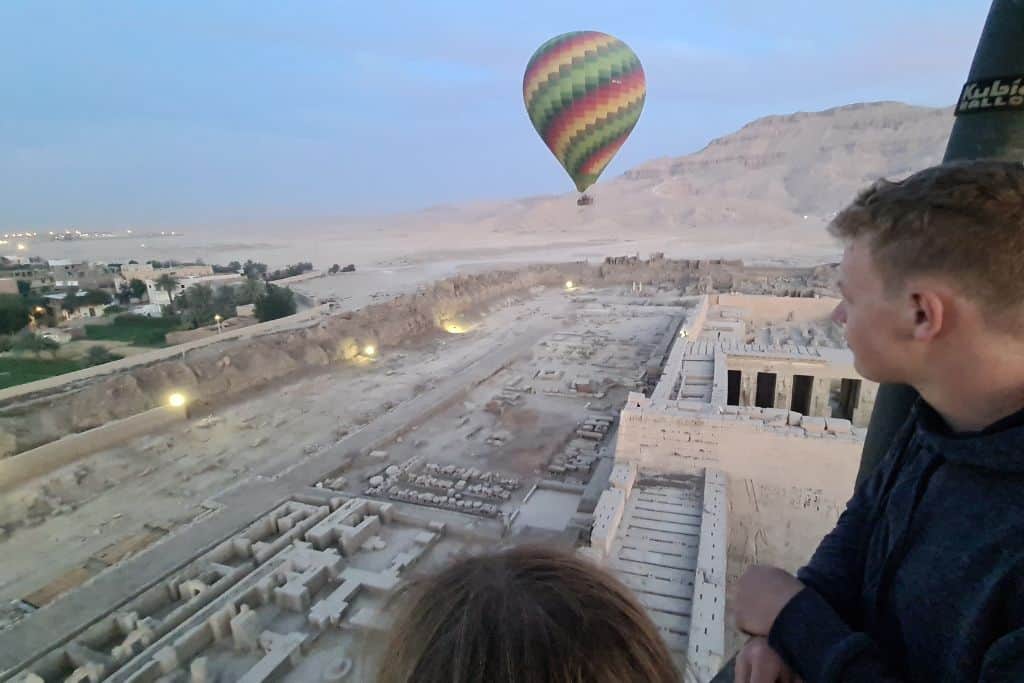 Kids floating in a hot air balloon with others over temples in the desert in Luxor, Egypt.