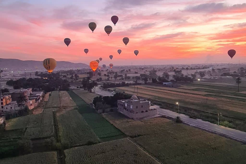 Multiple hot air balloons floating at sunrise over Luxor, Egypt.